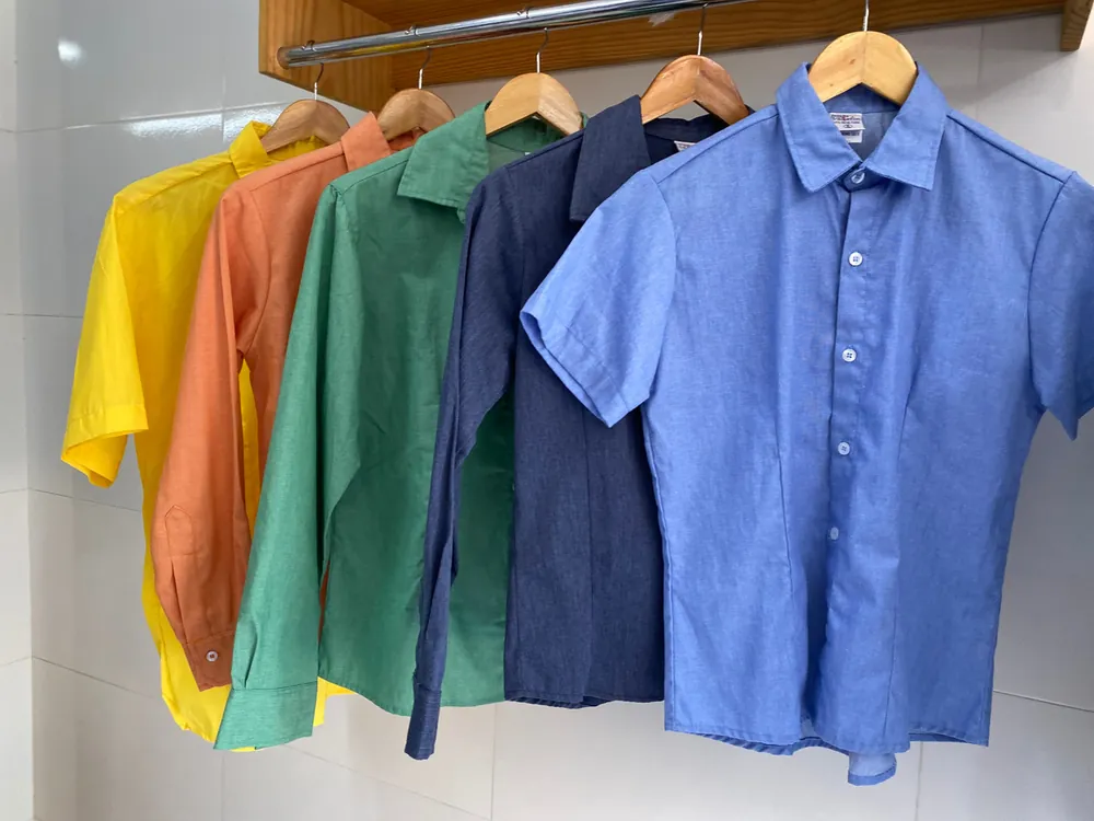 Cinco camisas sociais em cores diferentes (amarela, laranja, verde, azul-marinho e azul) penduradas em cabides